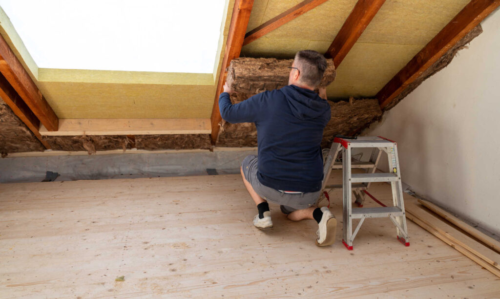 Handwerker verlegt Dämm-Material auf dem Dachboden